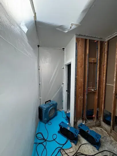 Containment and air movers drying an opened wall cavity in a home