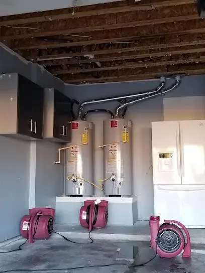 Air movers drying a garage floor set below two tank water heaters