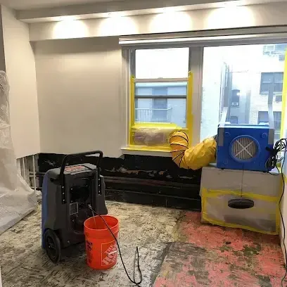 A dehumidifier and an air mover running side by side in a room where the flooring has been taken out