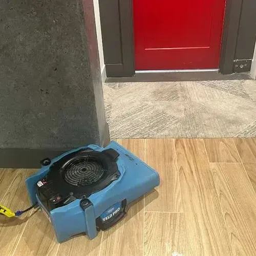 An air mover running across a wood-look tile floor beside an open doorway while the room dries out