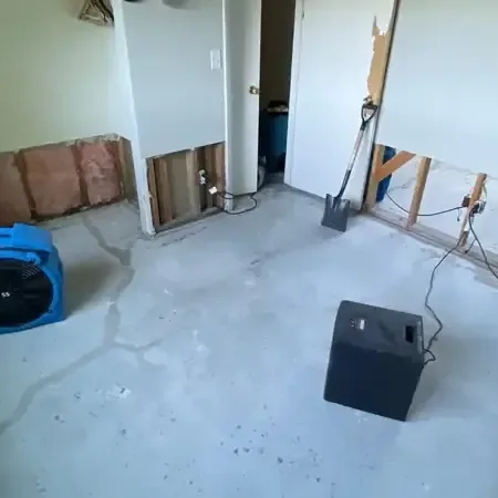A dehumidifier and air movers set up in a room with the lower drywall cut out and the bare floor drying