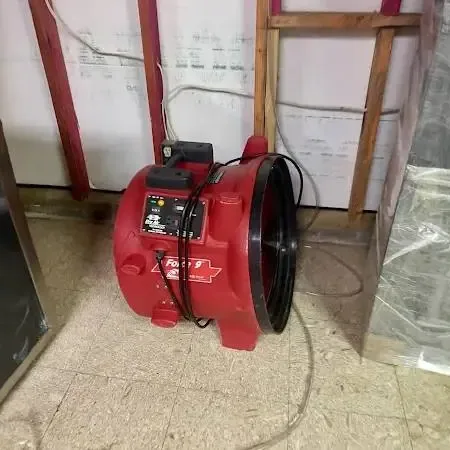 Red air mover drying a room with the lower wall opened and plastic sheeting hung after a floor leak